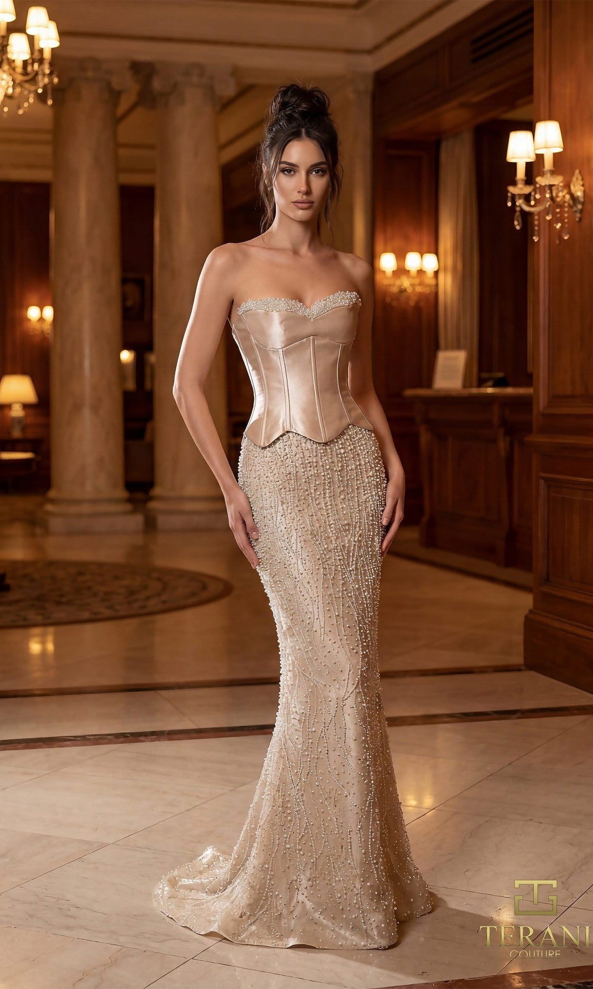A woman in a champagne Terani 261E6238 long formal dress with a pearl-embellished skirt stands in a warmly lit, marble-floored room featuring columns and wood paneling.